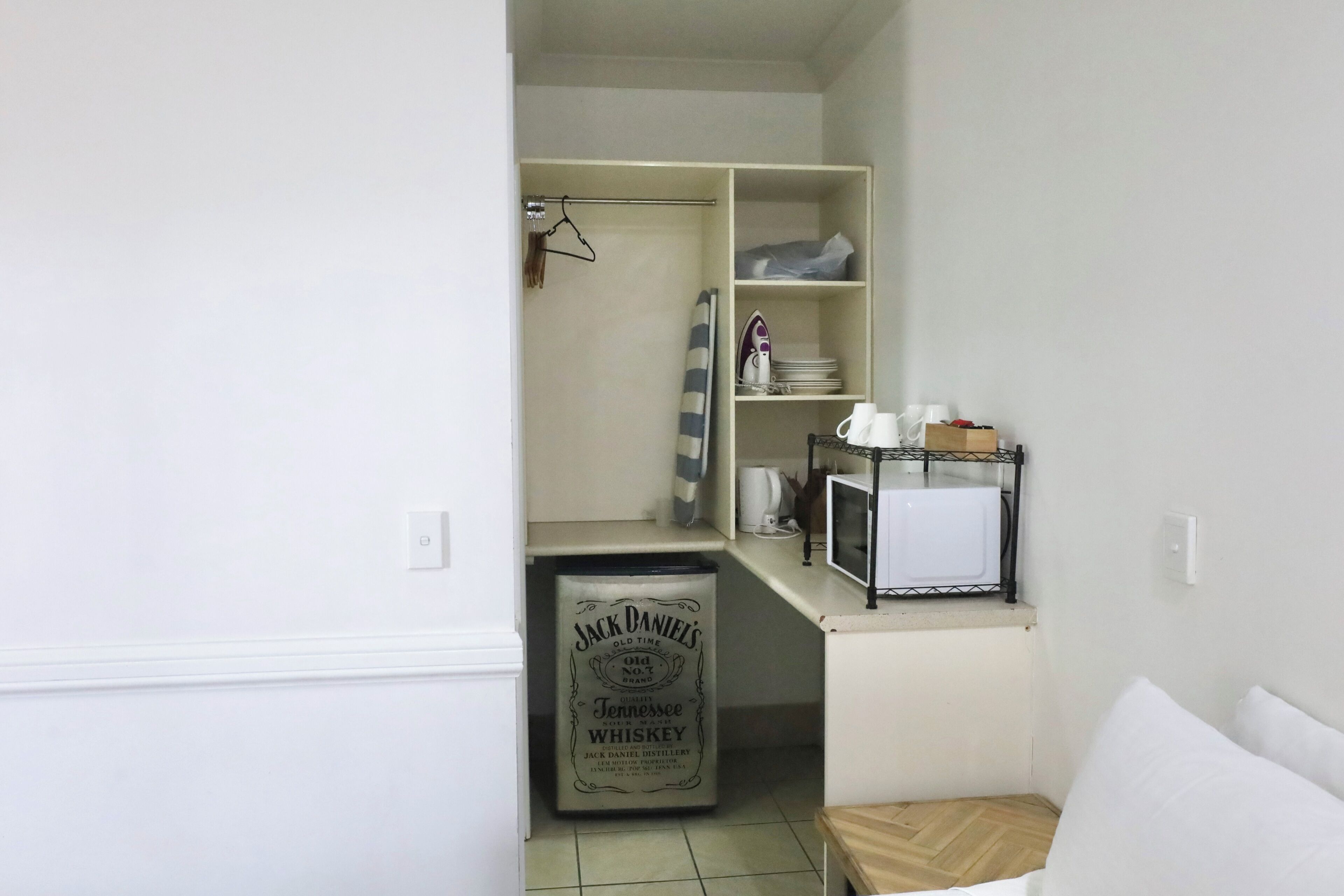 A compact kitchenette with a microwave, a coffee maker, and a hanging clothes rack.