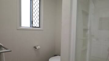 A small bathroom with a toilet, a window, and a shower curtain.