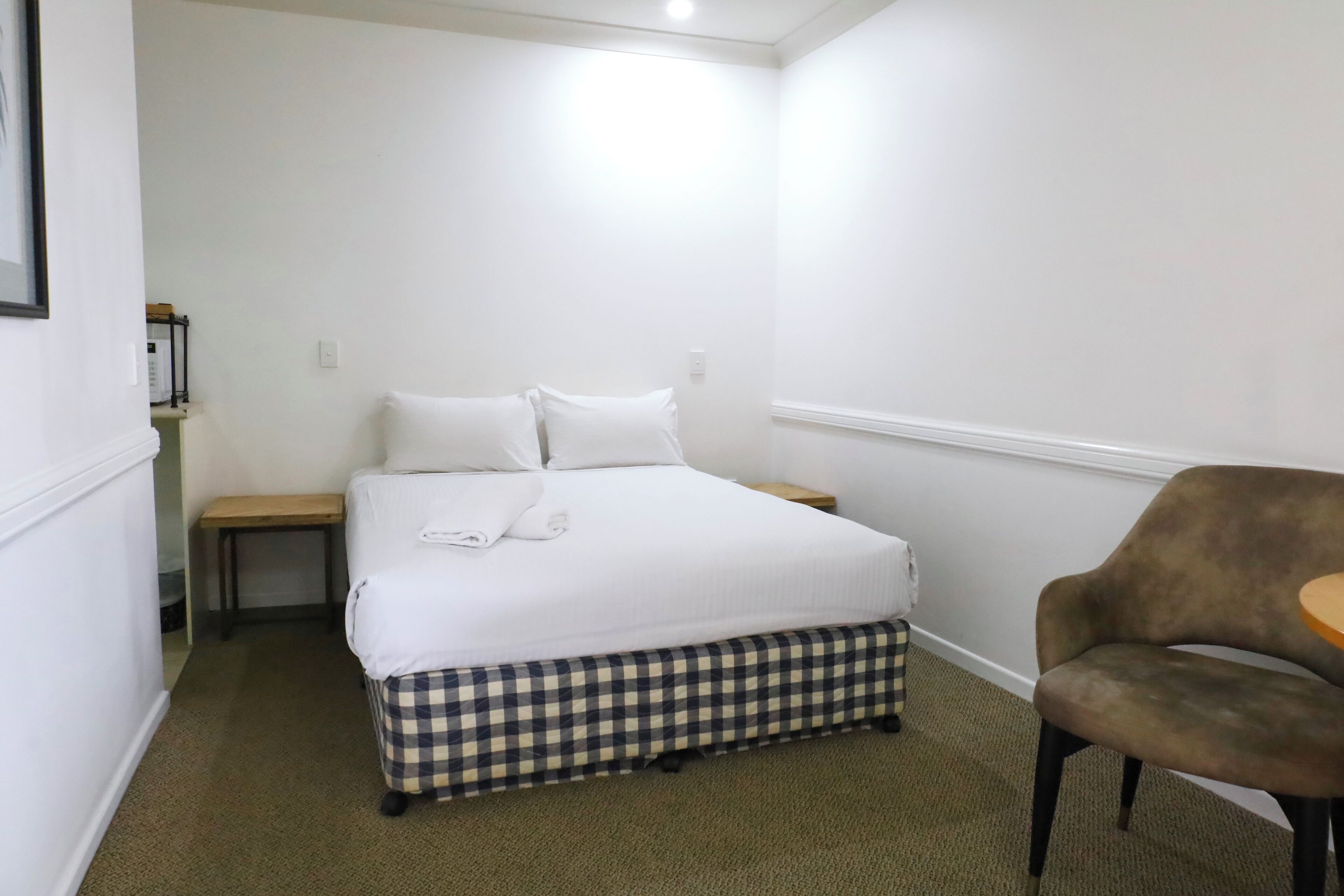 A bedroom with a bed, a chair, a small table, and a bench.