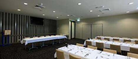 Un salón de conferencias con varias mesas dispuestas para comer, una pantalla grande y una puerta que da a otra habitación.