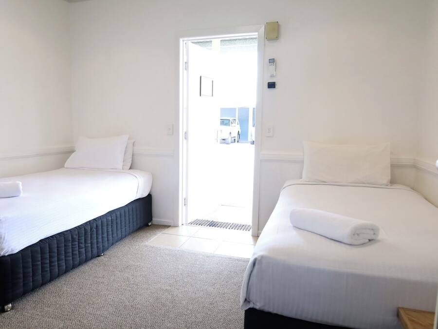 Una habitación con dos camas, cada una con ropa de cama y almohadas blancas, una alfombra gris y una puerta blanca que da al exterior.