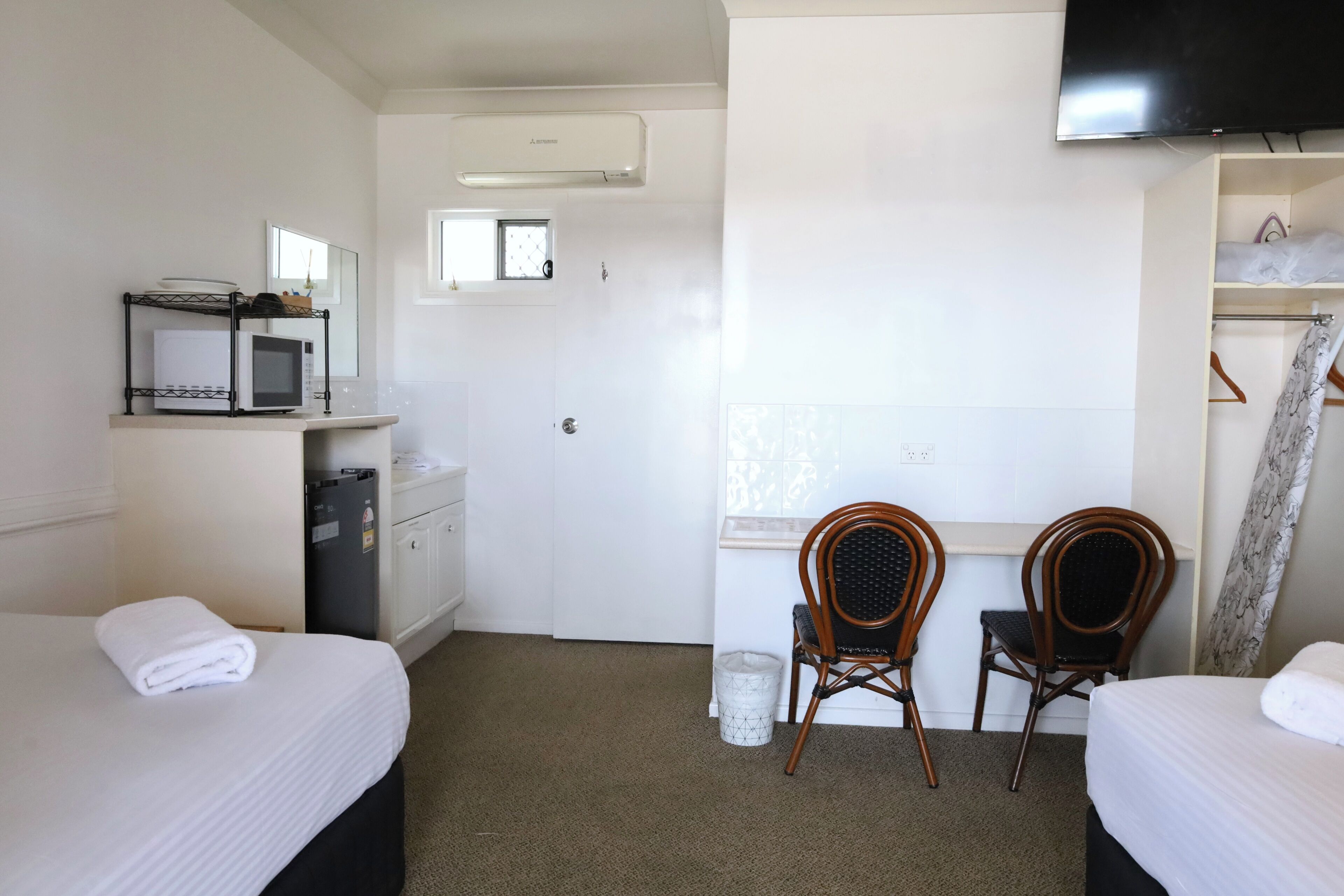 Ein Hotelzimmer mit zwei Betten, einem Schreibtisch mit Stuhl, einem Fernseher und einem Kleiderschrank.