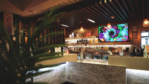 Een bar met een groot televisiescherm, flessen op de planken en een toonbank.