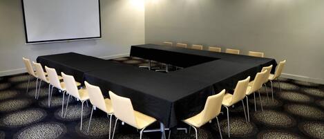 A conference room with a long table, chairs, a projector screen, and patterned carpet.