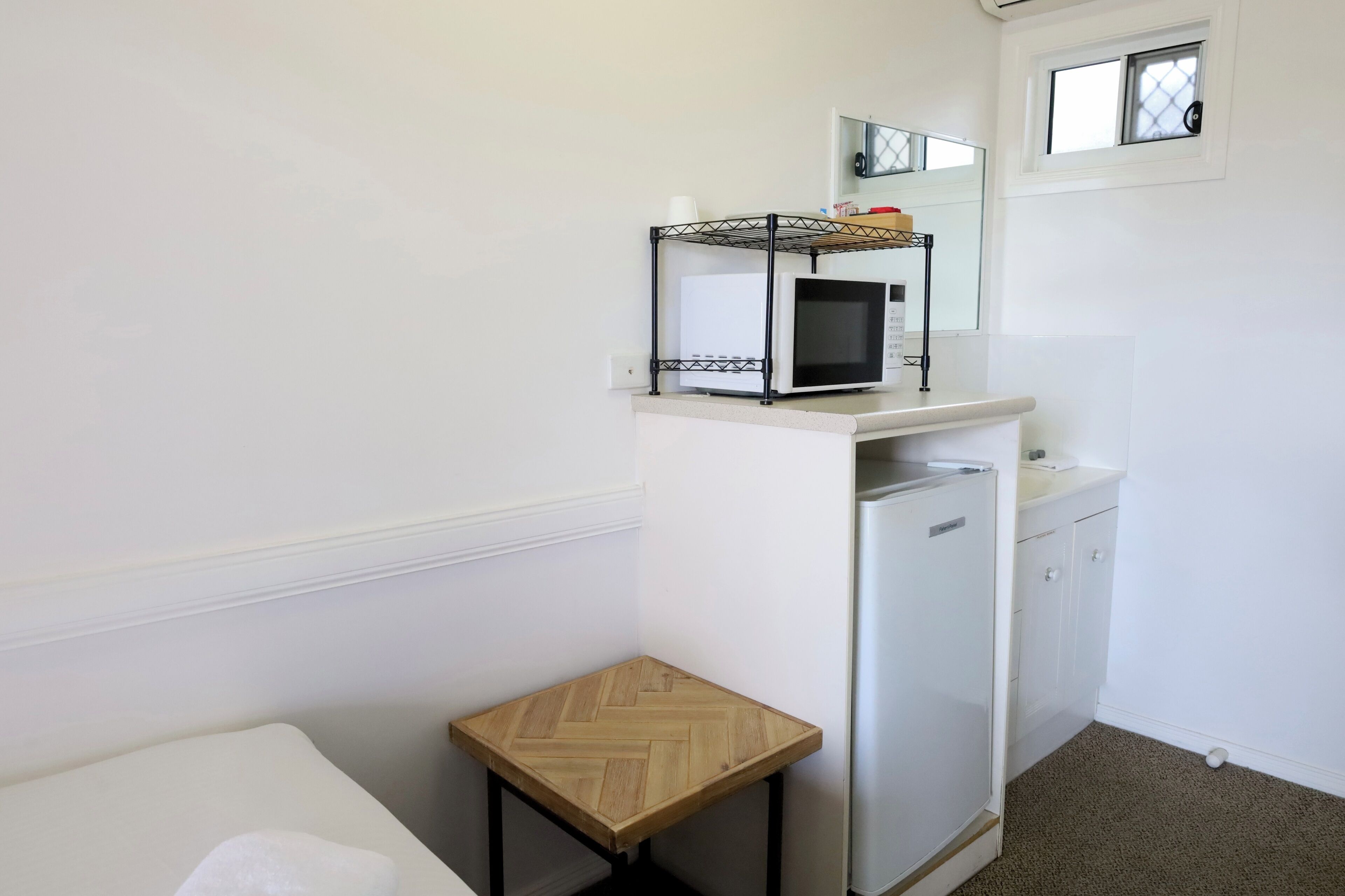 Una kitchenette compacta con microondas, un refrigerador pequeño y un taburete de madera.