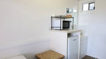 Una kitchenette compacta con microondas, un refrigerador pequeño y un taburete de madera.