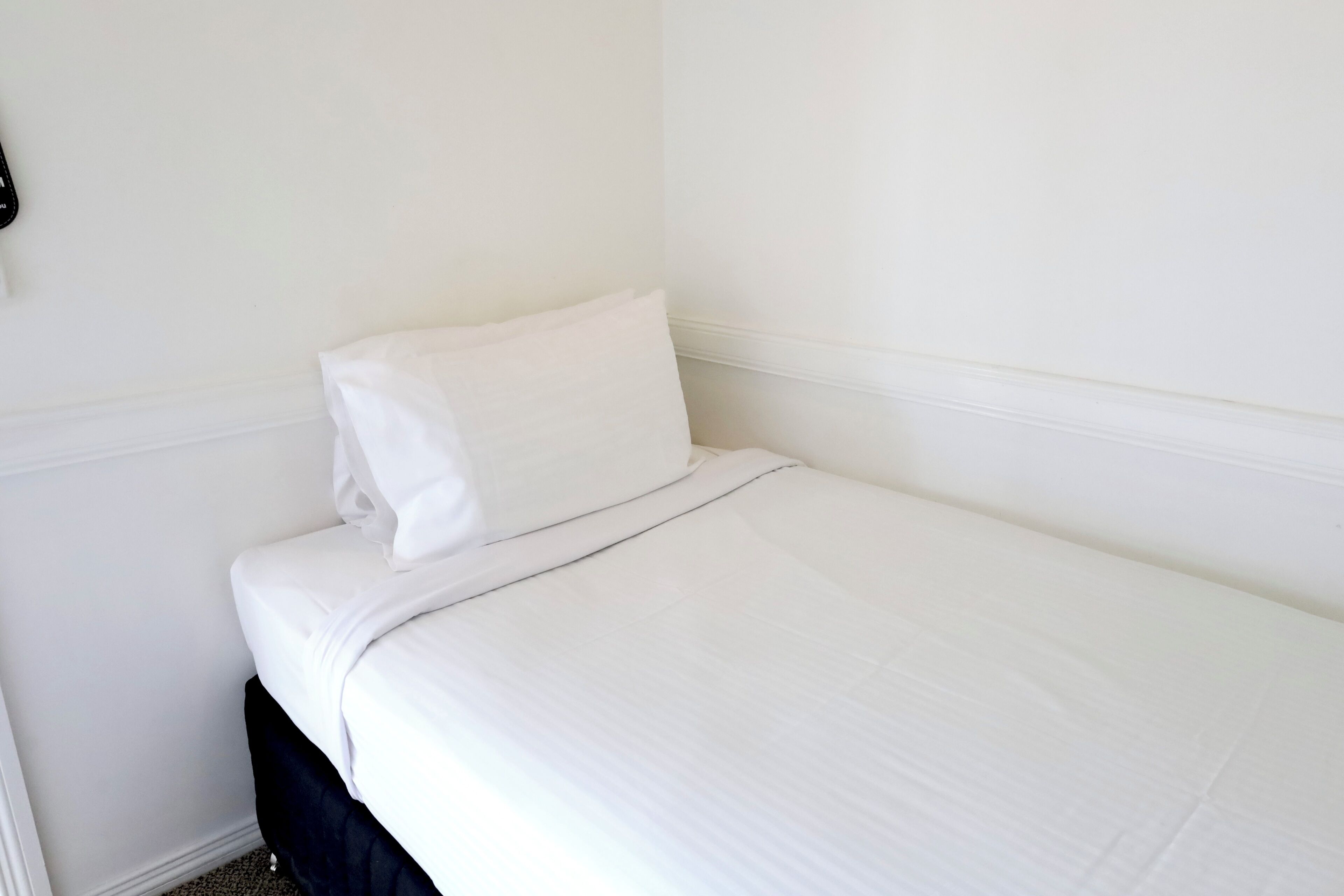 A small, neatly made bed with white bedding in a minimalistic room.