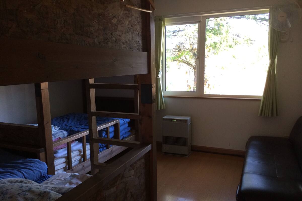 Ein Zimmer mit Etagenbetten, einer Heizung, einem Fenster mit Vorhängen und einem Sofa.