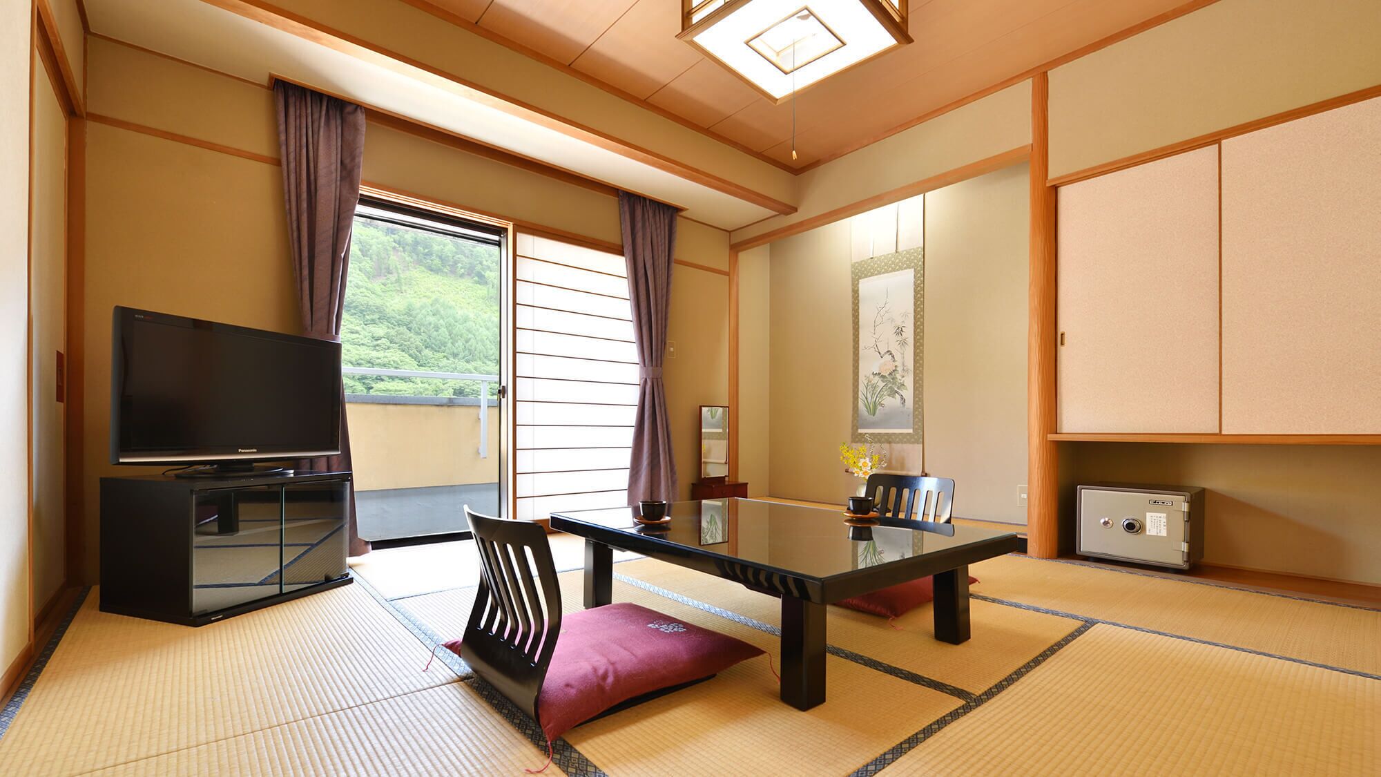 A traditional Japanese room with tatami flooring, a television, a table with chairs, and a sliding door leading to a balcony.