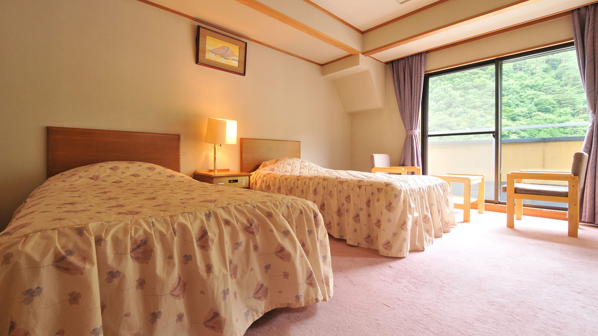 A hotel room with two beds, a nightstand, a lamp, a chair, and a large window with a view of greenery.