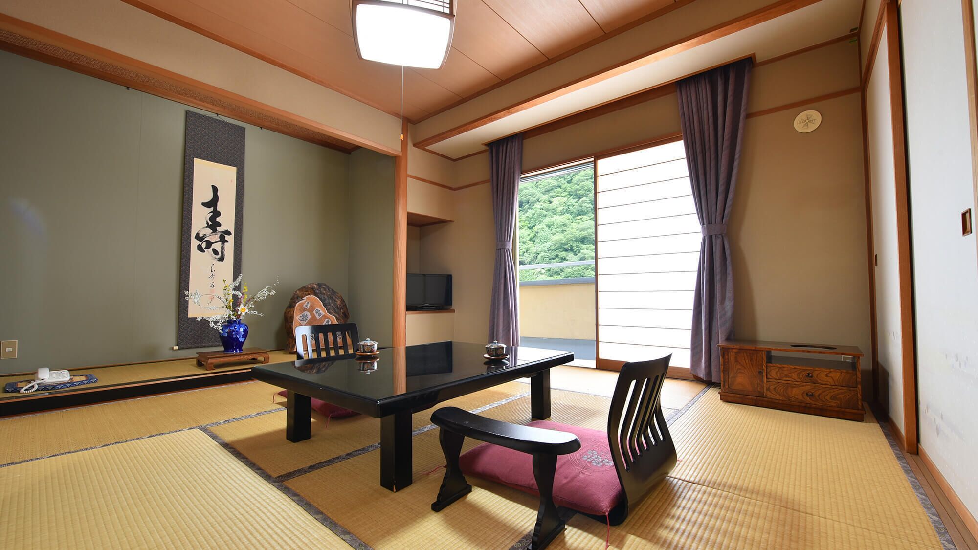Una habitación japonesa tradicional con suelo de tatami, una mesa baja, un banco, un televisor y una puerta corrediza con vistas a la vegetación.