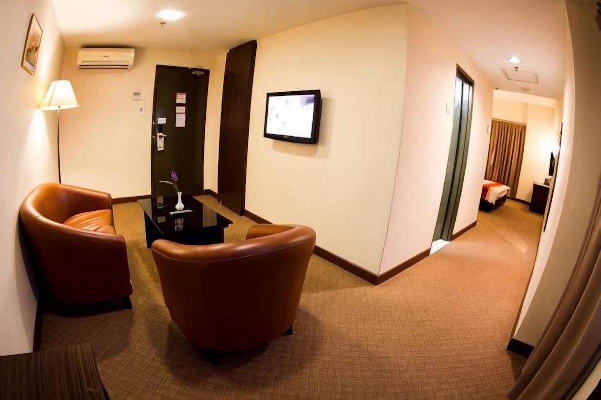 Un vestíbulo de hotel con sillones de cuero, un mostrador de recepción, un televisor de pantalla plana y una puerta que da a un dormitorio.