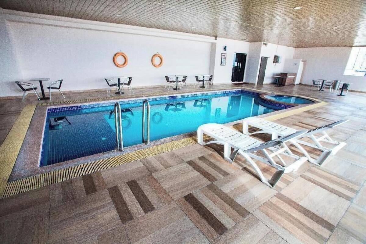 Una piscina interior con suelo de baldosas, sillas junto a la piscina y techo de ladrillo.