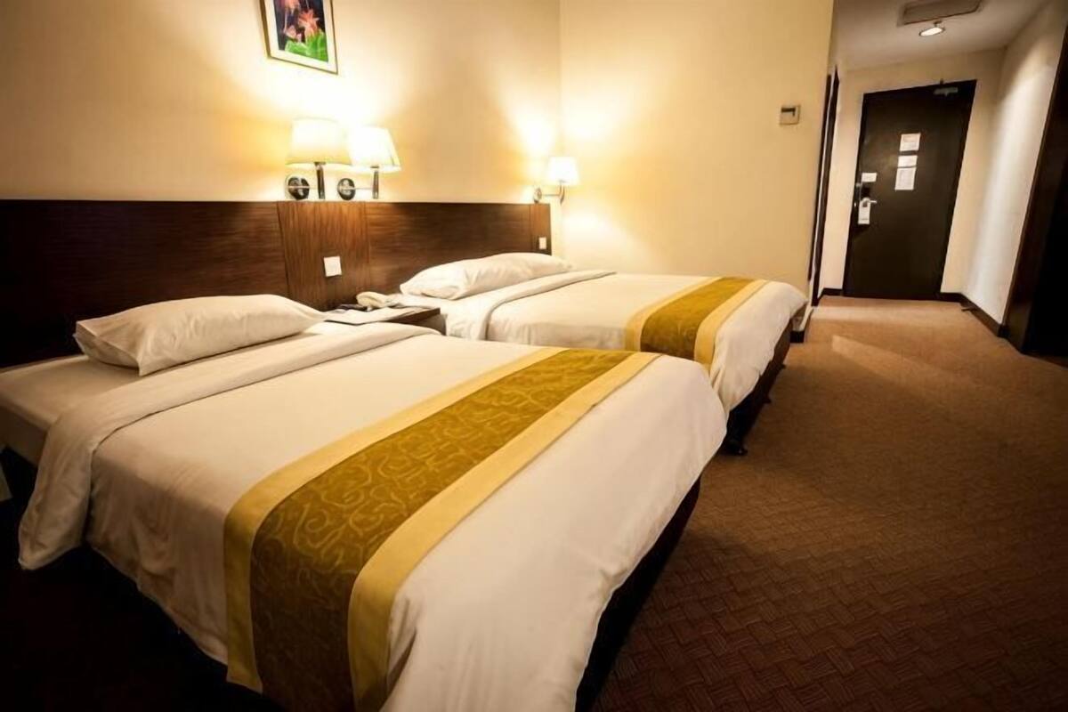 Habitación de hotel con dos camas, cabecero, lámparas fijadas a la pared y suelo alfombrado.