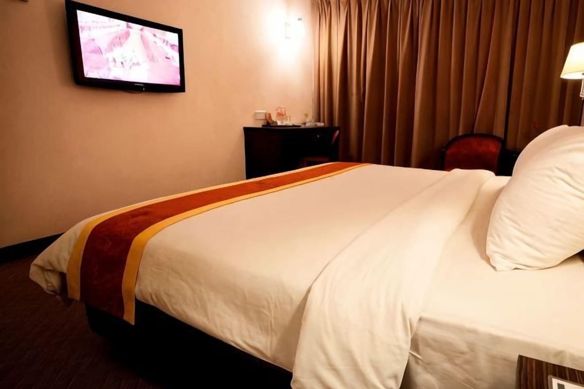 Habitación de hotel con cama, televisión montada en la pared, escritorio con lámpara y una silla.
