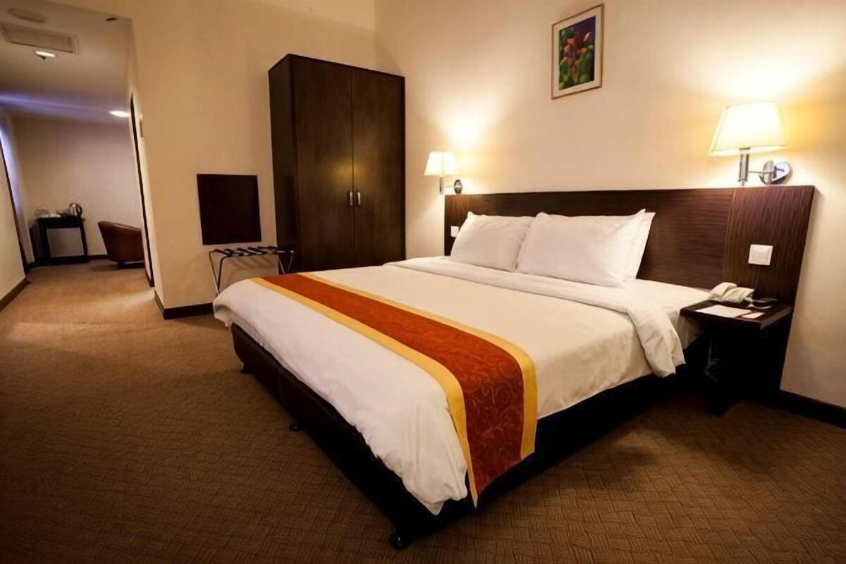 Habitación de hotel con una cama grande, un armario de madera, un escritorio con silla y dos lámparas de noche.