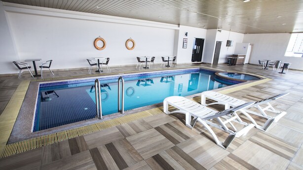 An indoor swimming pool with tiled flooring, lounge chairs, and tables.