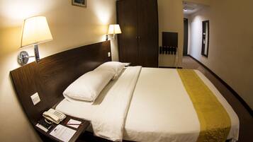 A hotel room with a large bed, two bedside lamps, a telephone, and a desk with a notepad and pen.