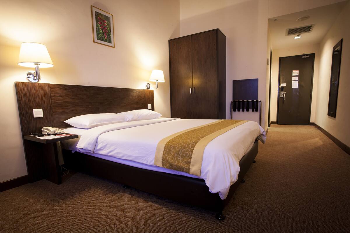 Una habitación de hotel con una cama grande, dos lámparas de noche, un armario y una puerta que da a otra habitación.