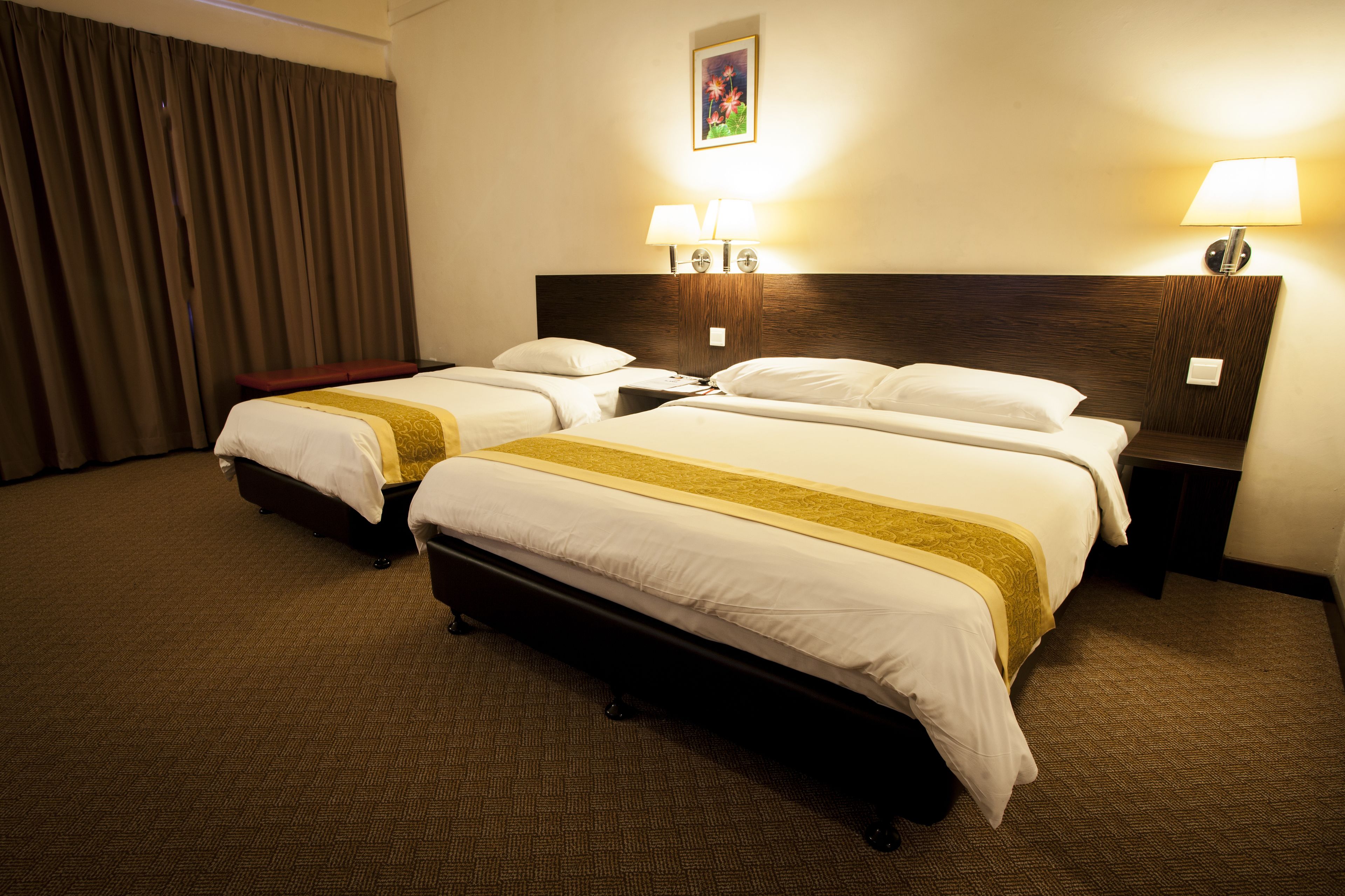 A hotel room with two beds, a wooden headboard, a nightstand with lamps, and a large window with curtains.