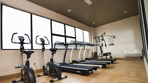 A gym with stationary bikes and treadmills, large windows, and a wooden floor.