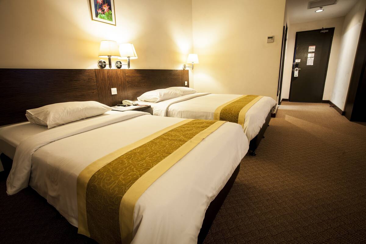Una habitación de hotel con dos camas, cabeceros, lámparas de noche, suelo alfombrado y una puerta.