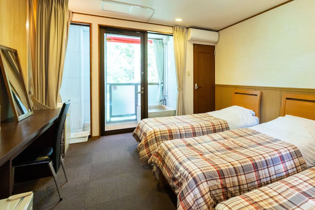 A hotel room with two beds, a desk, and a sliding door leading to an outdoor area.