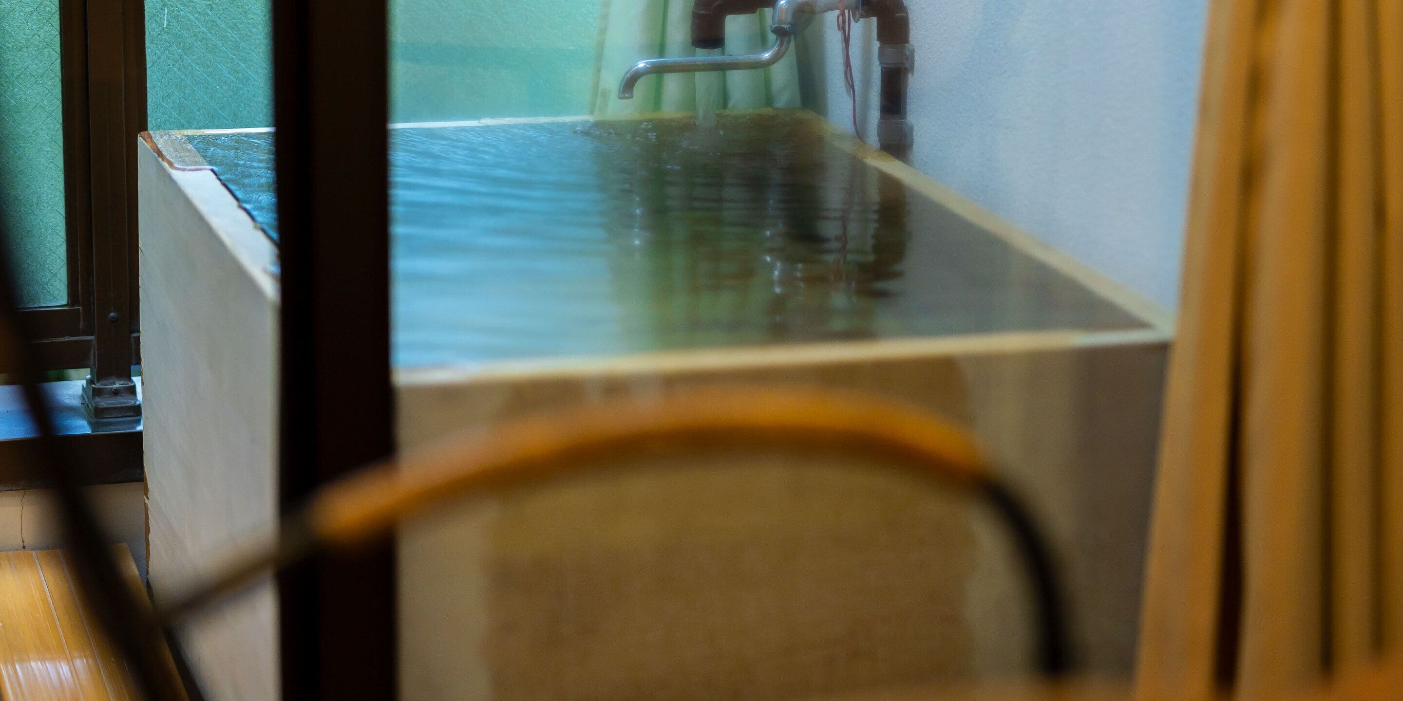 A room with a large window, a wooden floor, and a visible water pipe.