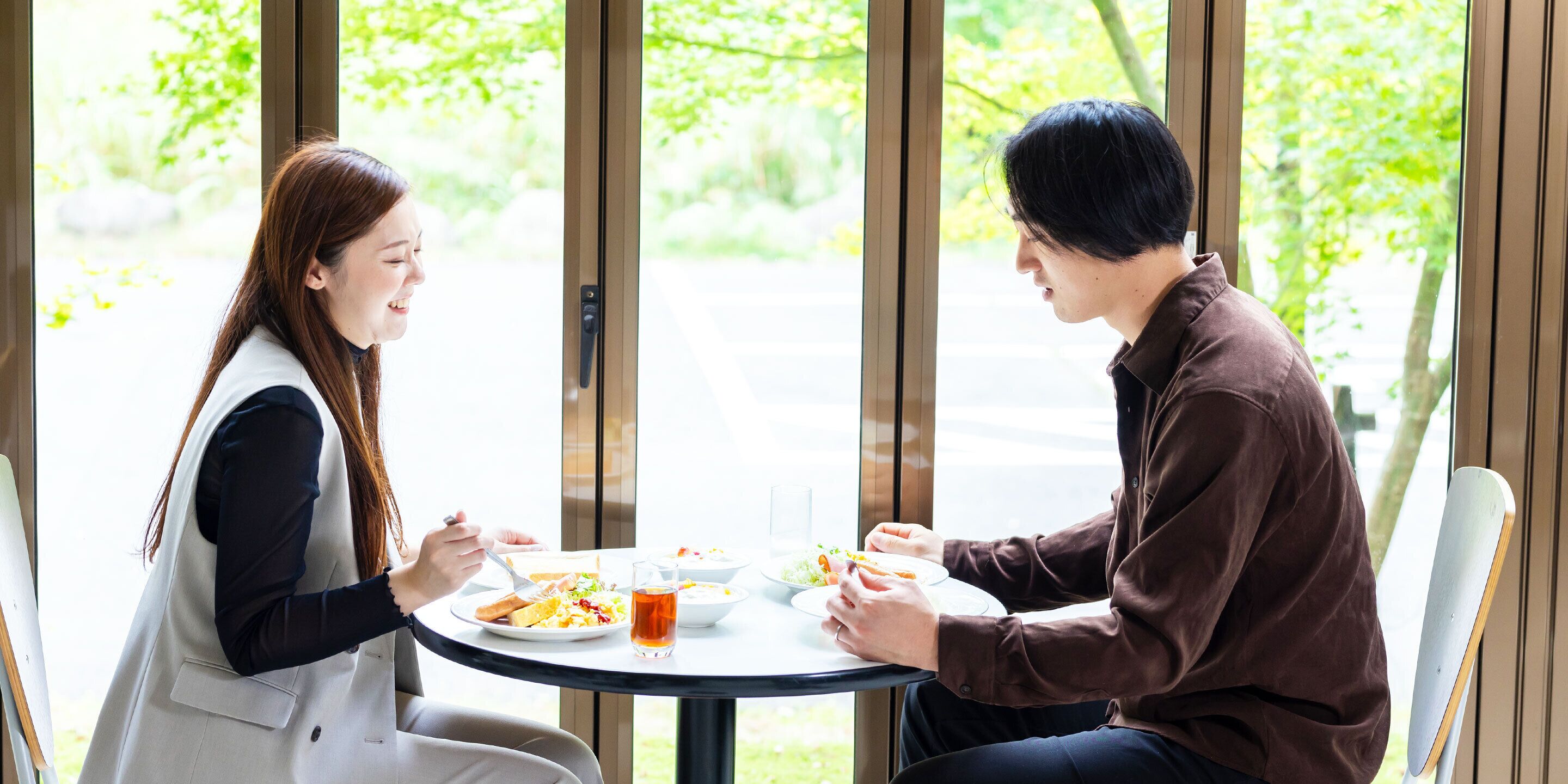 Two people dining at a round table with a view of greenery outside.