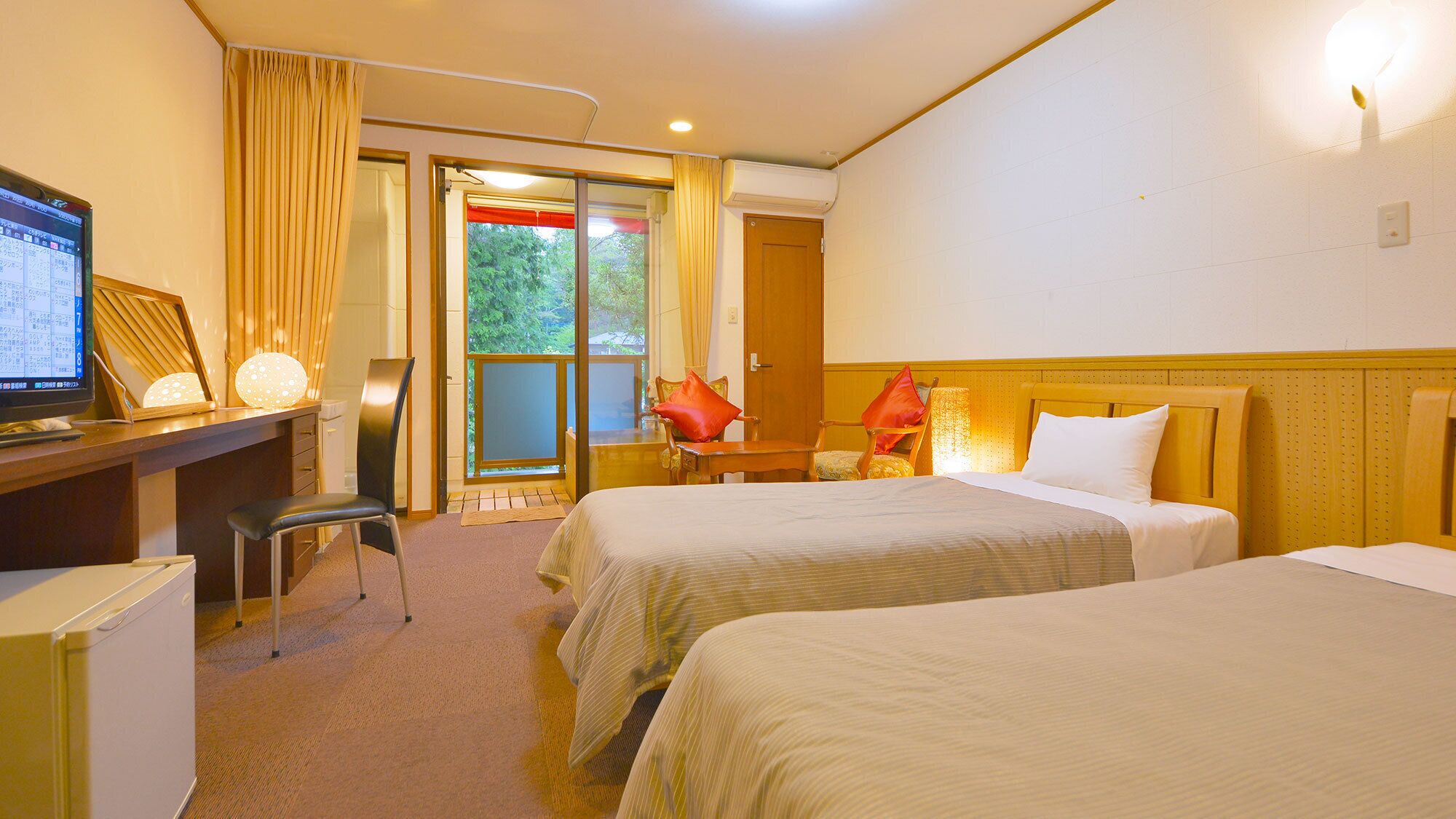 Habitación de hotel con dos camas, un escritorio con computadora, una silla y vista a zonas verdes.