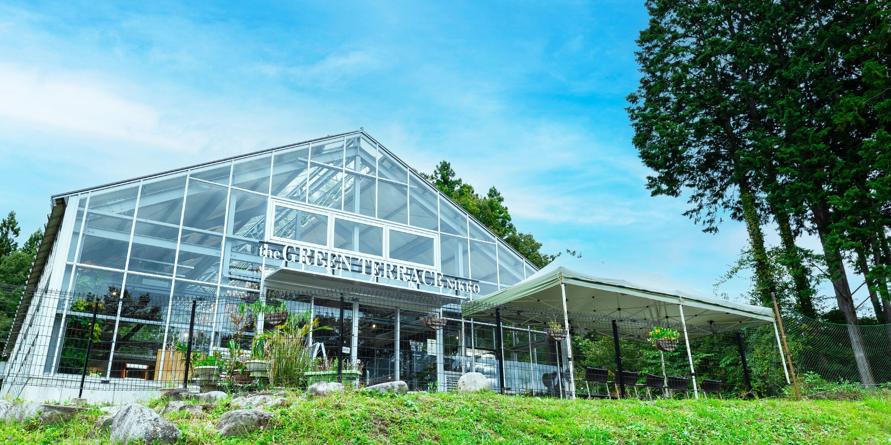 A large greenhouse with a transparent roof, surrounded by greenery and trees.