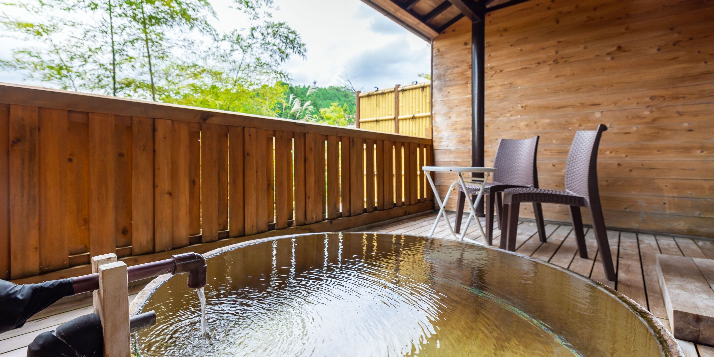 Una terraza de madera con un jacuzzi de fondo de cristal, sillas de madera y una mesa.