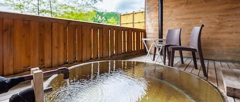 A wooden deck with a glass-bottomed hot tub, wooden chairs, and a table.