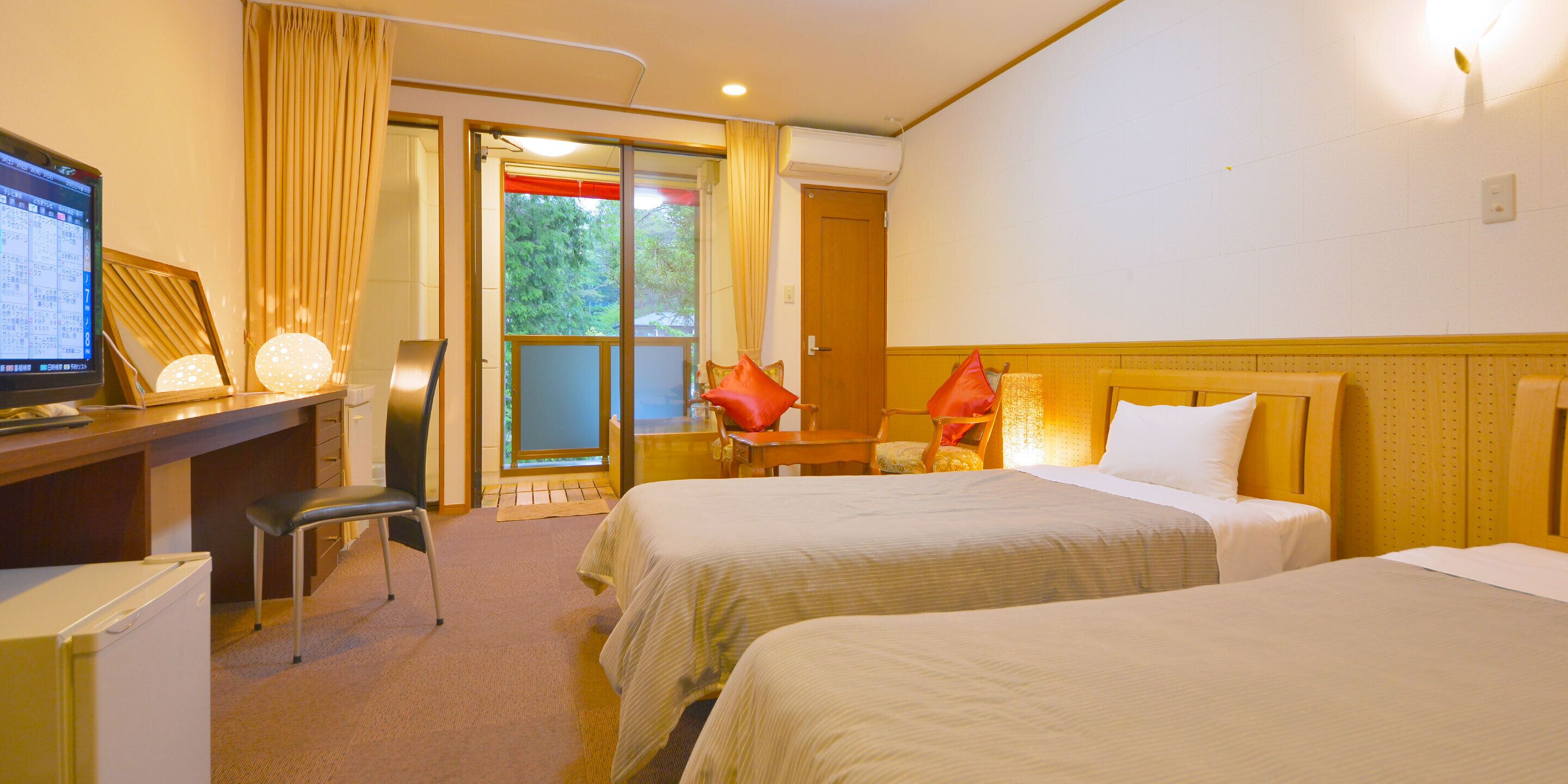 Une chambre d’hôtel avec deux lits, un bureau avec un ordinateur, une chaise et une vue sur l’extérieur grâce à une porte coulissante.