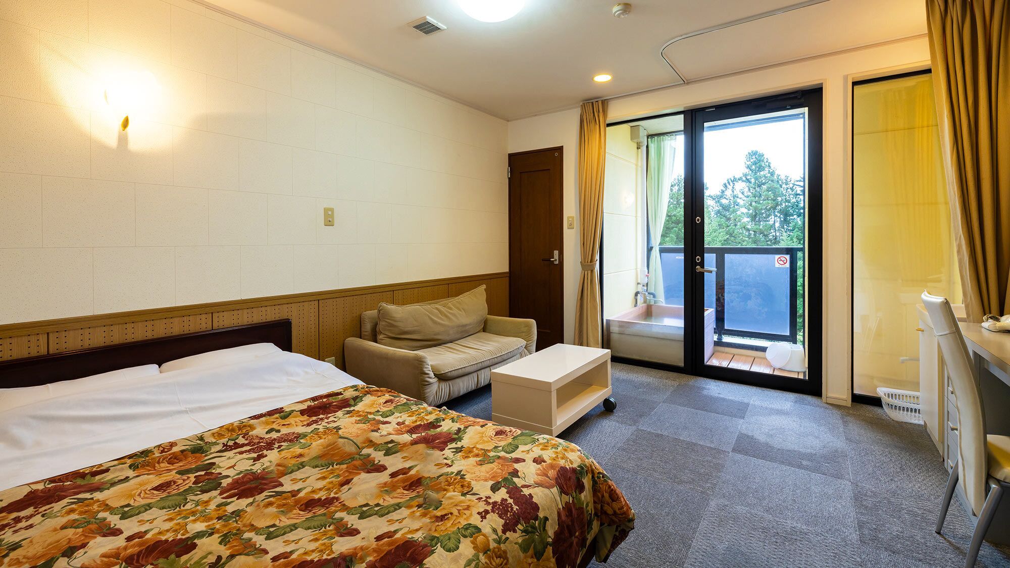 Habitación de hotel con cama, sofá, una mesita y una puerta corredera de vidrio que da a un espacio exterior.