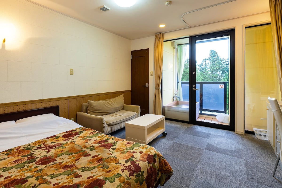 Een hotelkamer met een bed, een slaapbank, een kleine tafel en een schuifdeur naar een buitenruimte.