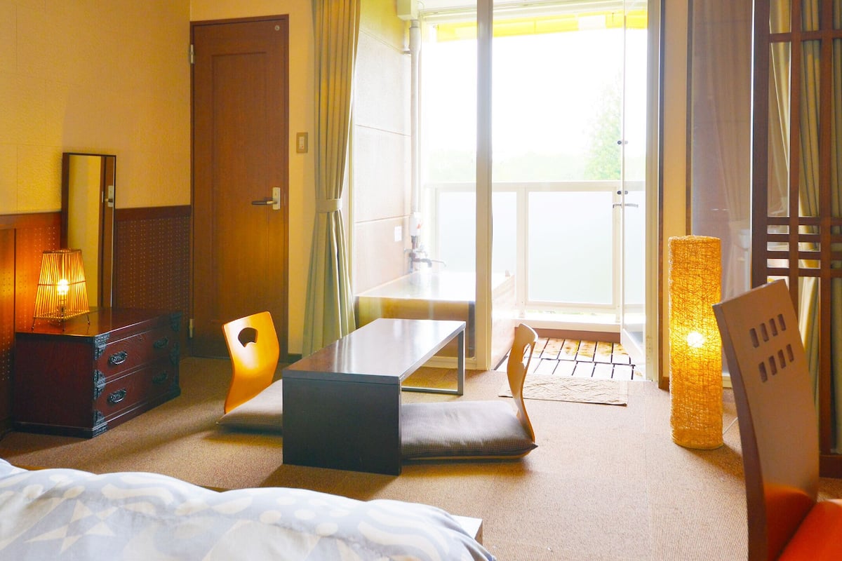 A hotel room with a bed, a desk, a chair, a TV, and a window with a view of the outdoors.