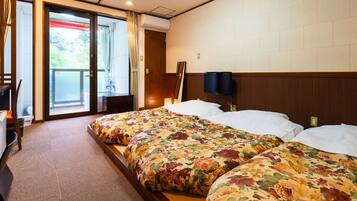 Quarto de hotel com duas camas, uma escrivaninha, uma cadeira e televisão fixada na parede.