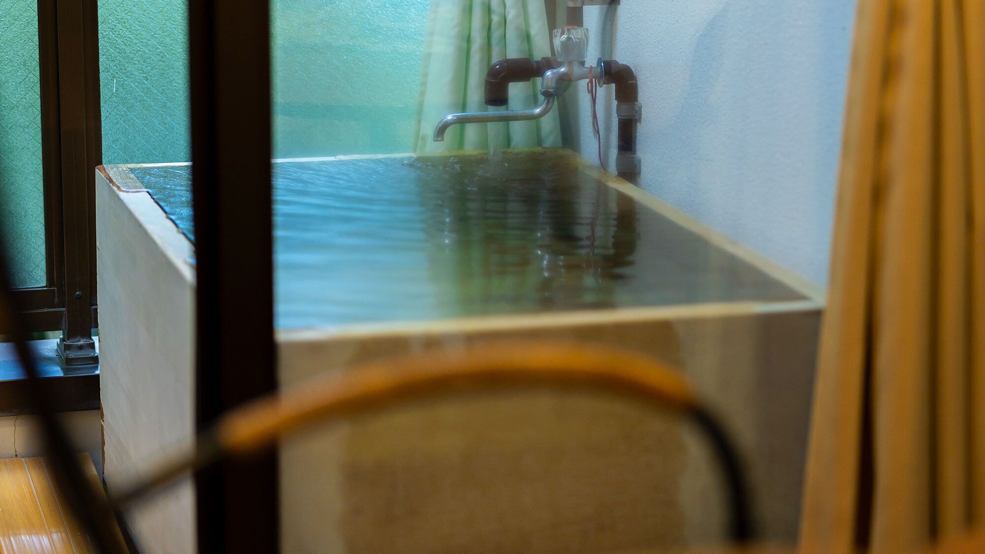 Habitació amb finestra, sòl de fusta i un element de fontaneria visible.