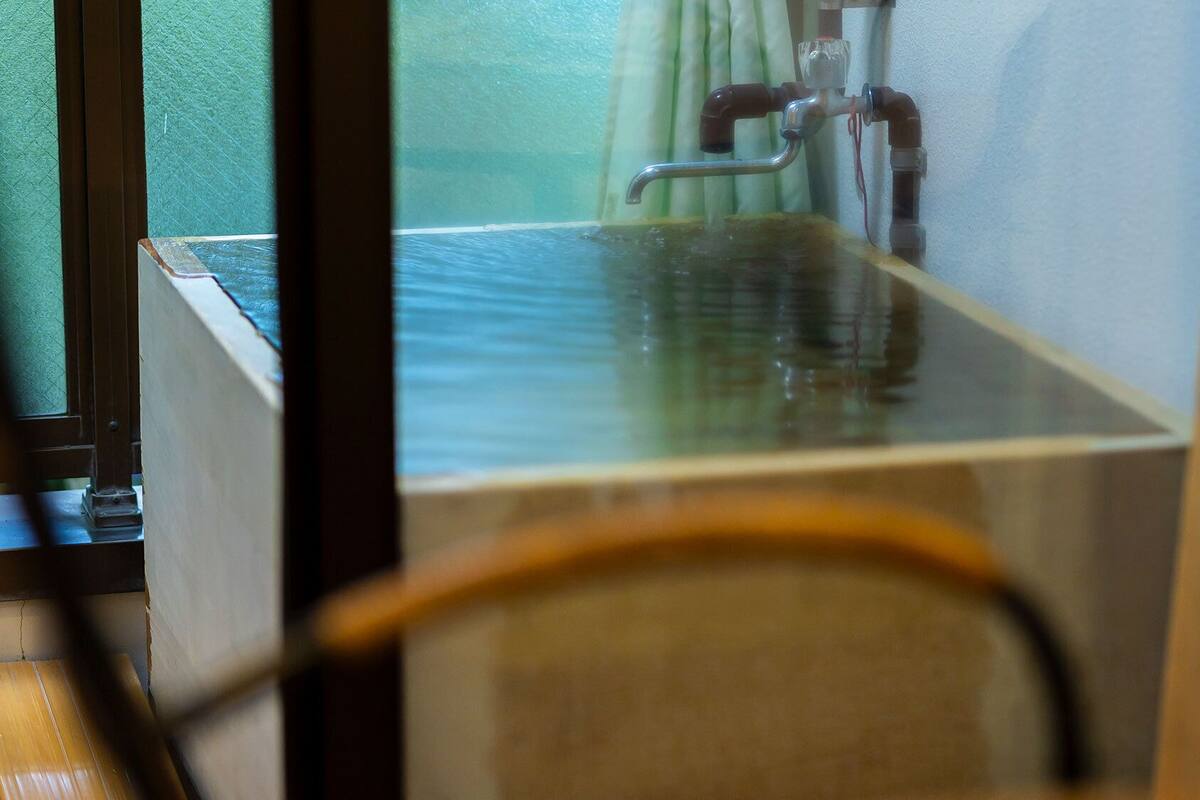 A room with a window, a wooden floor, and a visible plumbing fixture.