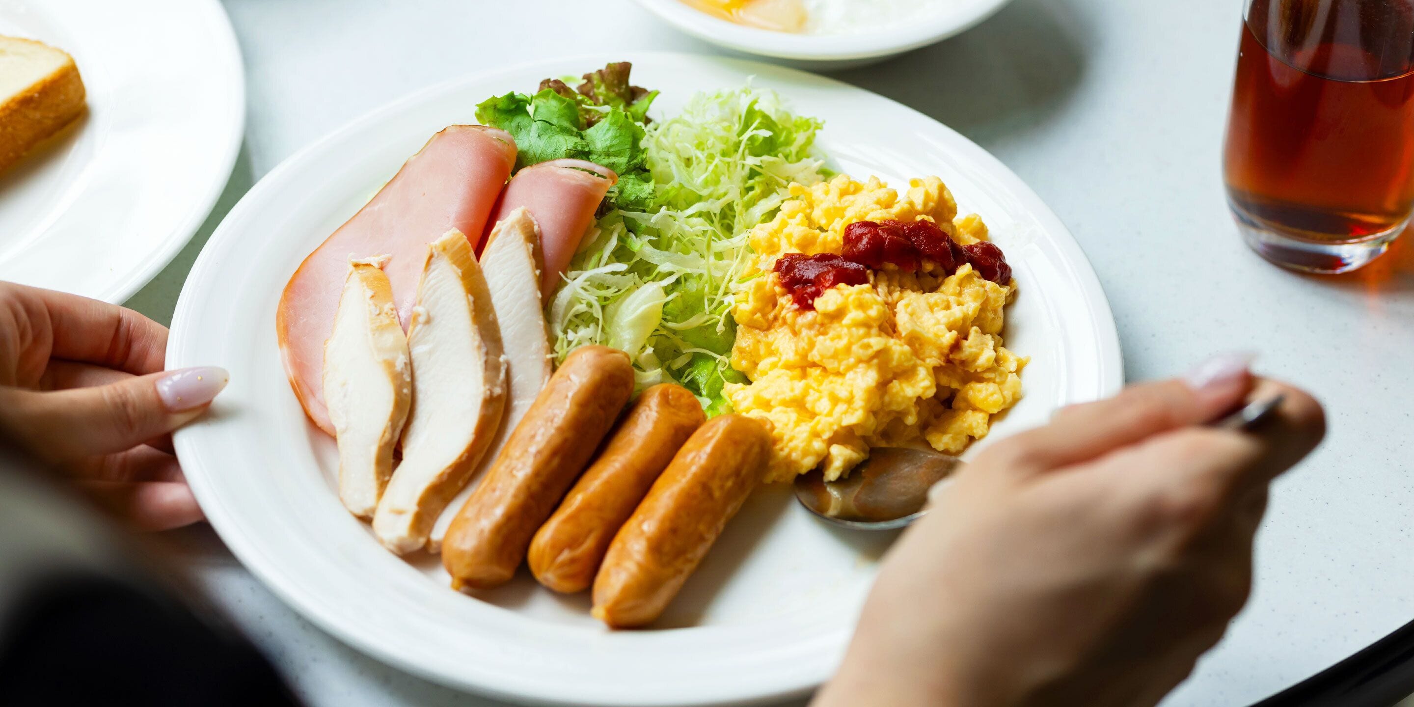 A plate with sliced ham, sausages, scrambled eggs, and lettuce.