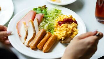 A plate with sliced ham, sausages, scrambled eggs, and lettuce.