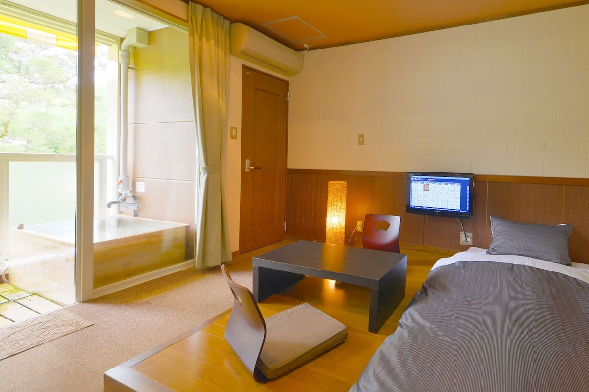 A hotel room with a bed, a desk, a chair, a television, and a sliding glass door to the outside.