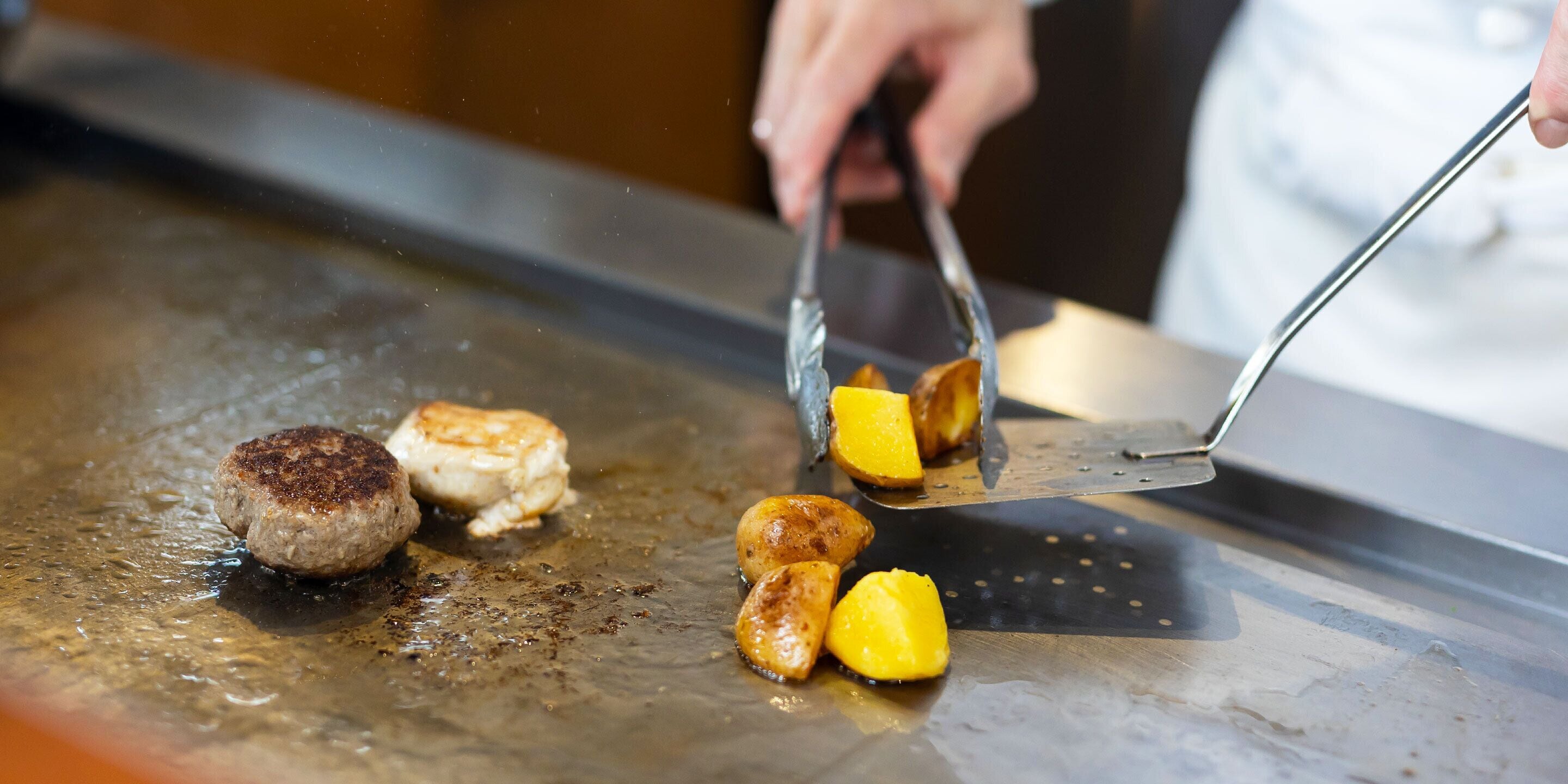 A cooking surface with a patty and pieces of fruit being cooked.