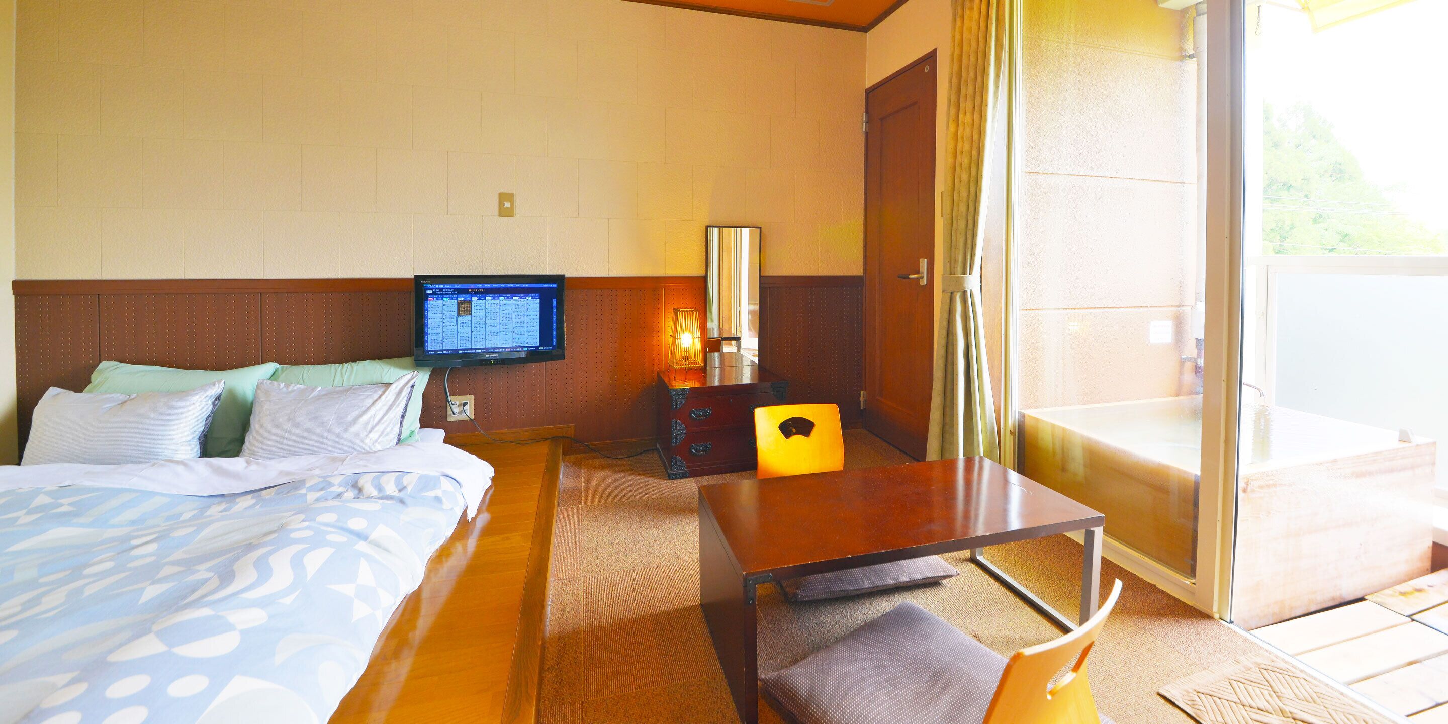 Habitación de hotel con cama, escritorio, silla, televisión y puerta corrediza al balcón.