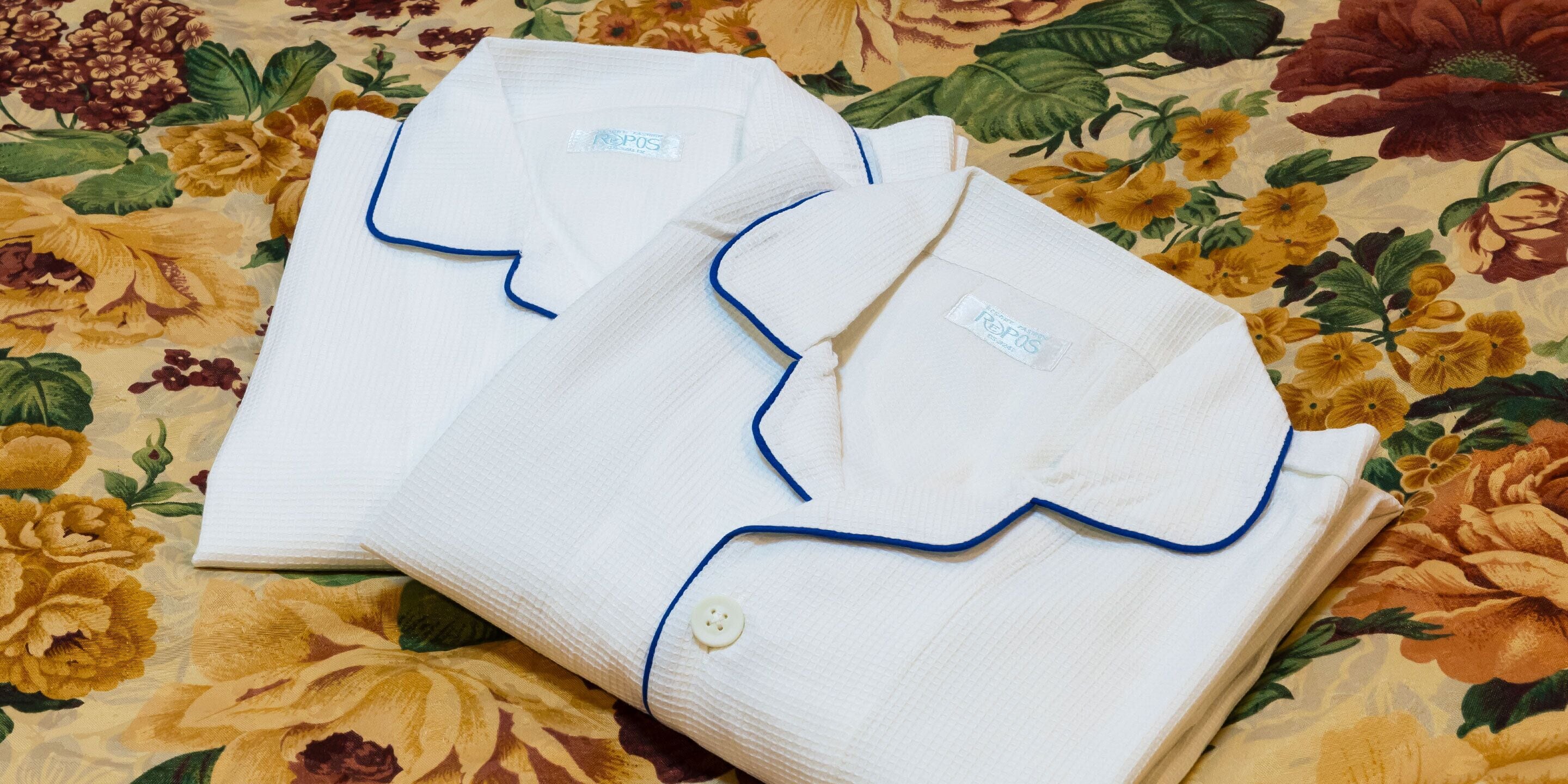 Una camicia bianca ordinatamente piegata, con risvolto blu e un bottone, poggiata su un tessuto a motivi floreali.