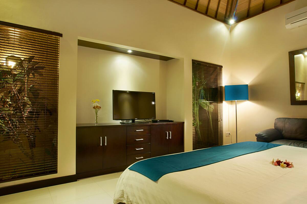 A modern bedroom with a bed, a TV on a cabinet, a lamp, and a large mirror.