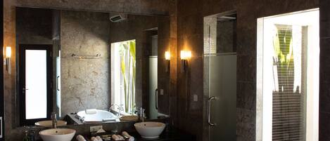 A bathroom with a large bathtub, two sinks, a mirror, and a window with a view of greenery.