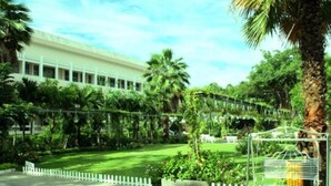 A building with a white facade, surrounded by lush greenery and palm trees. - Cuu Long Hotel (Can Tho)