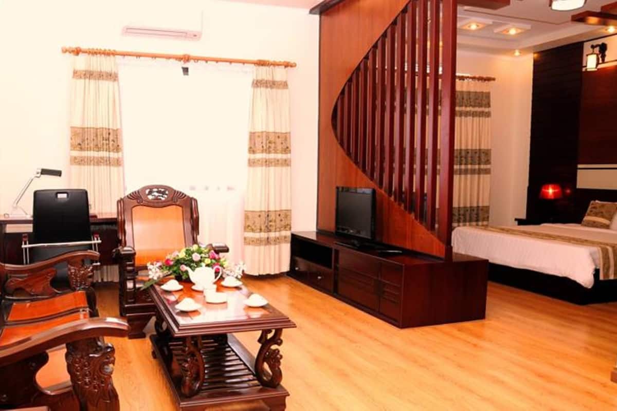 Una habitación con sofá de madera, un escritorio con computadora, un televisor y una cama con cabecera de madera.